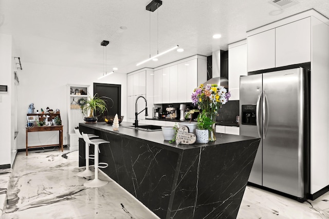 kitchen featuring white cabinetry, sink, stainless steel fridge with ice dispenser, decorative light fixtures, and a kitchen bar