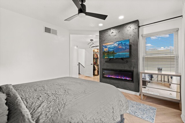 bedroom with a large fireplace, ceiling fan, and light hardwood / wood-style floors