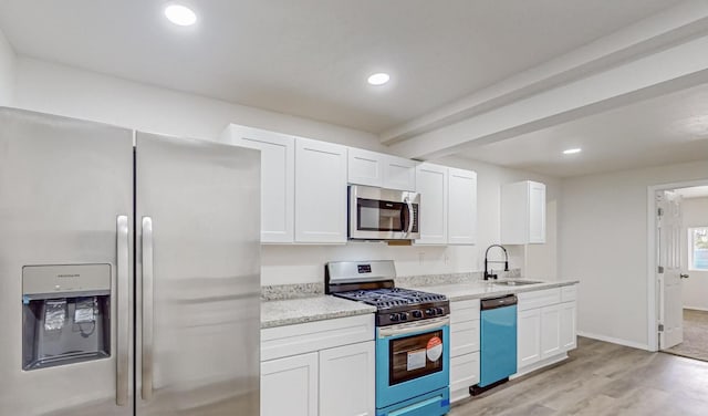 kitchen with sink, light wood-type flooring, appliances with stainless steel finishes, light stone counters, and white cabinetry