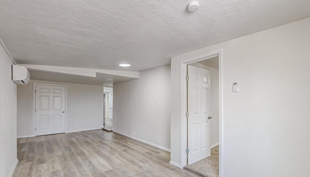 basement featuring a wall mounted air conditioner, a textured ceiling, and light hardwood / wood-style flooring