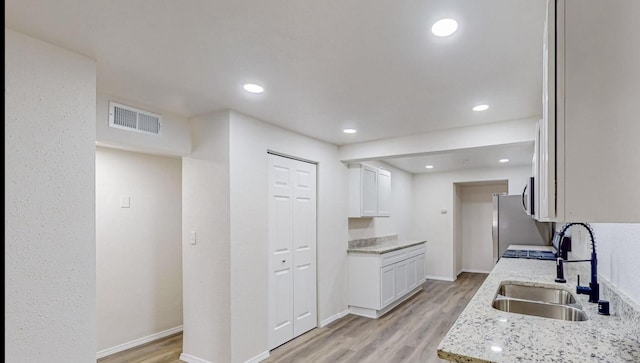 kitchen featuring white cabinets, light wood-type flooring, light stone countertops, and sink