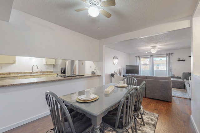 dining space featuring ceiling fan, sink, dark wood-type flooring, and a textured ceiling