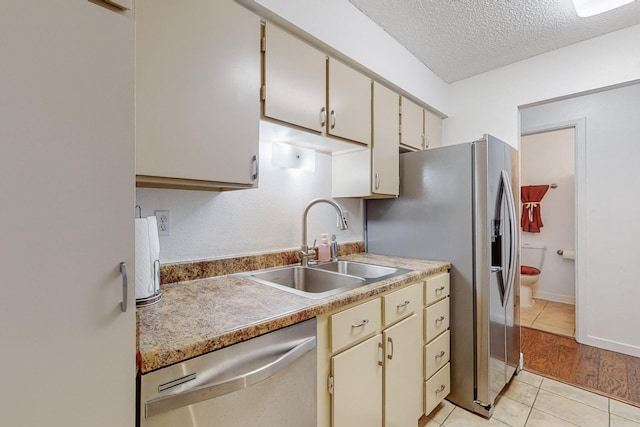 kitchen with sink, cream cabinets, light hardwood / wood-style floors, a textured ceiling, and appliances with stainless steel finishes