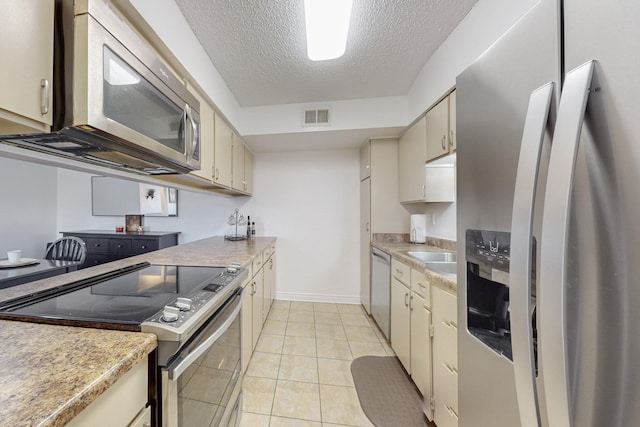 kitchen with light tile patterned floors, cream cabinetry, a textured ceiling, and appliances with stainless steel finishes