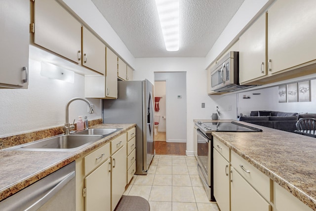 kitchen featuring a textured ceiling, stainless steel appliances, sink, light tile patterned floors, and cream cabinets