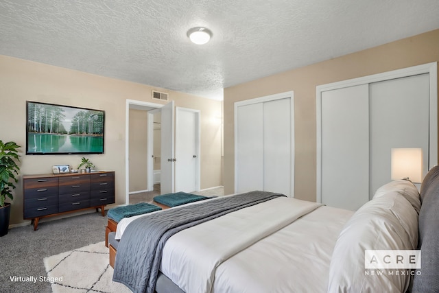 carpeted bedroom featuring a textured ceiling and two closets