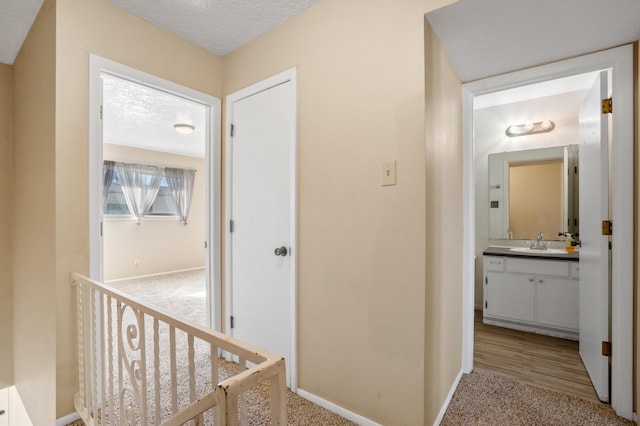 hallway with sink, light wood-type flooring, and a textured ceiling