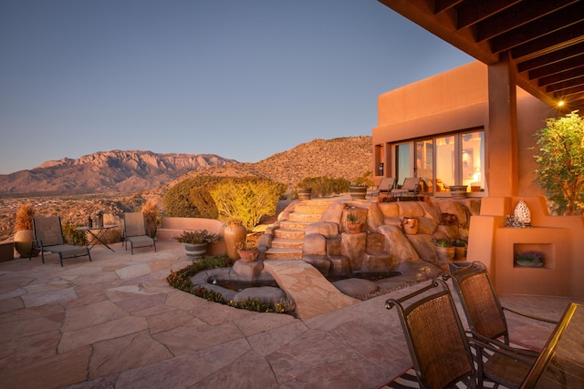 patio terrace at dusk featuring a mountain view and an outdoor fireplace