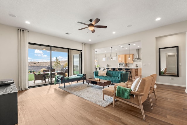 living room with ceiling fan, a textured ceiling, and light hardwood / wood-style flooring