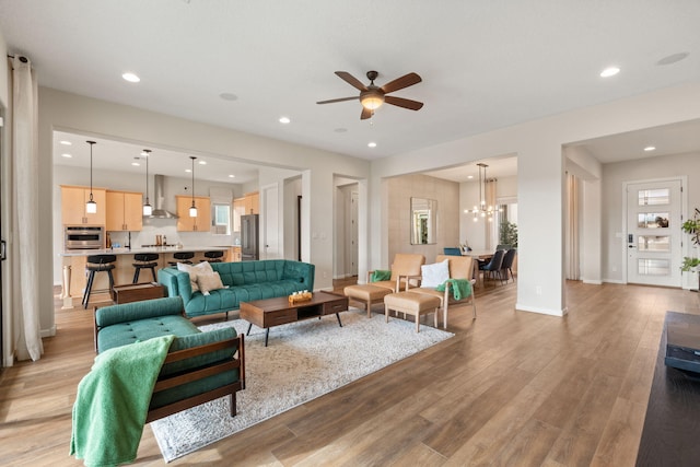 living room with ceiling fan with notable chandelier and light hardwood / wood-style floors