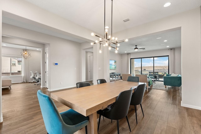 dining area with hardwood / wood-style floors, a healthy amount of sunlight, and ceiling fan with notable chandelier