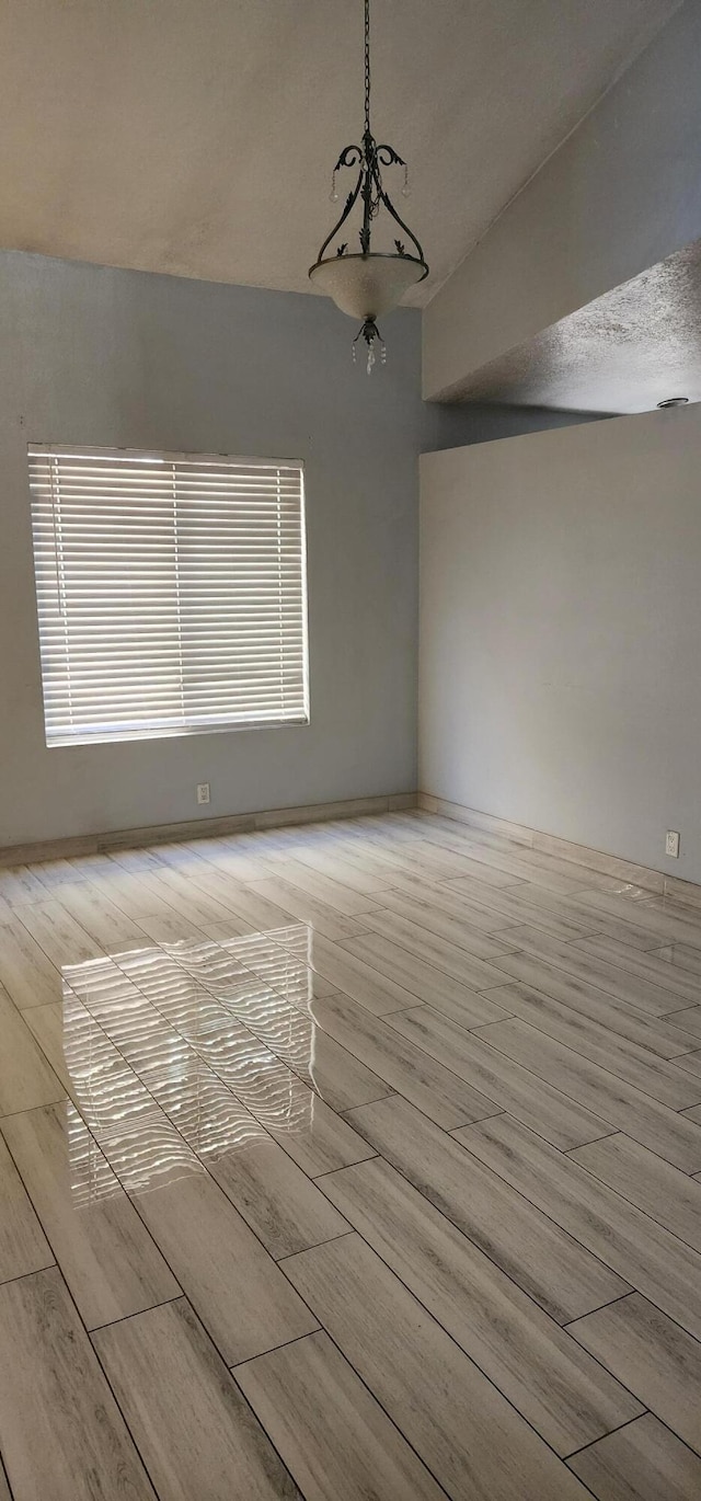 spare room featuring lofted ceiling, light hardwood / wood-style floors, and a textured ceiling