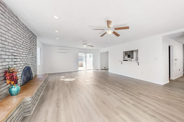 unfurnished living room with an AC wall unit, ceiling fan, a fireplace, and light wood-type flooring