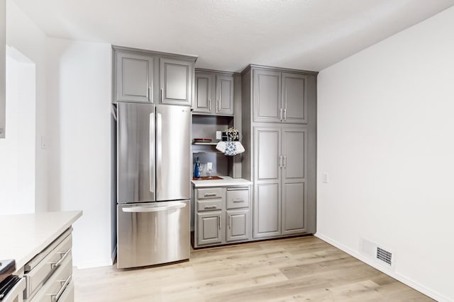 kitchen featuring gray cabinetry, stainless steel fridge, a textured ceiling, light hardwood / wood-style floors, and range