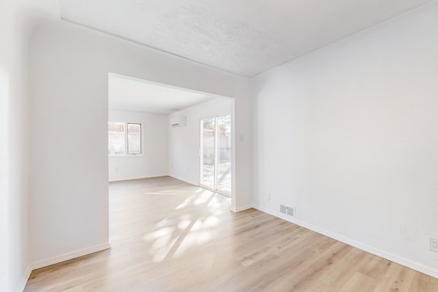 empty room featuring a textured ceiling, a wall unit AC, and light hardwood / wood-style flooring