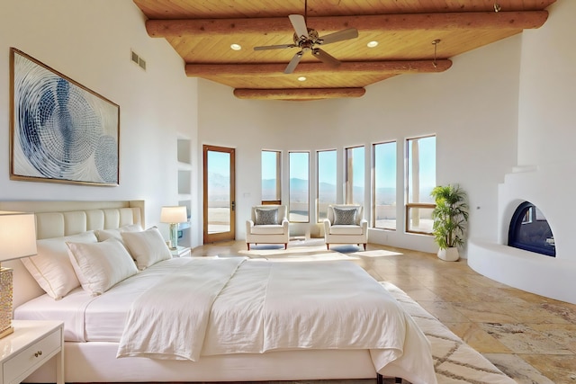 bedroom with visible vents, a towering ceiling, wood ceiling, beam ceiling, and a glass covered fireplace