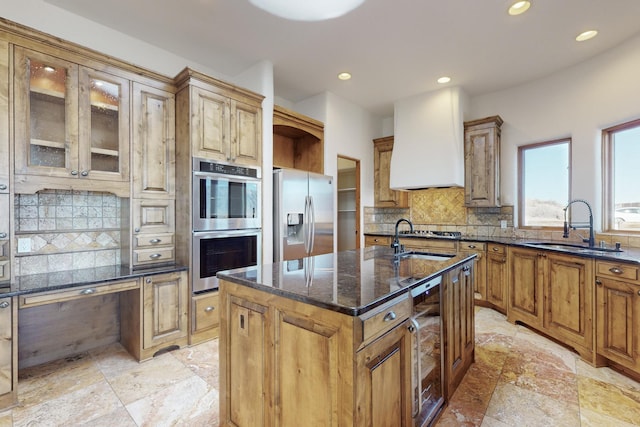 kitchen with wall chimney exhaust hood, wine cooler, appliances with stainless steel finishes, dark stone countertops, and a sink