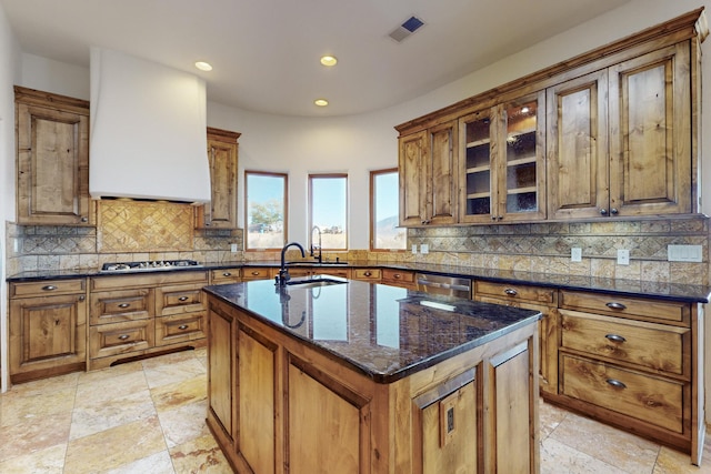 kitchen featuring a kitchen island with sink, a sink, visible vents, tasteful backsplash, and brown cabinetry