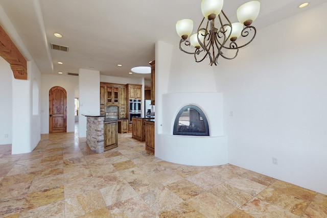 kitchen featuring dark countertops, visible vents, brown cabinetry, glass insert cabinets, and a multi sided fireplace