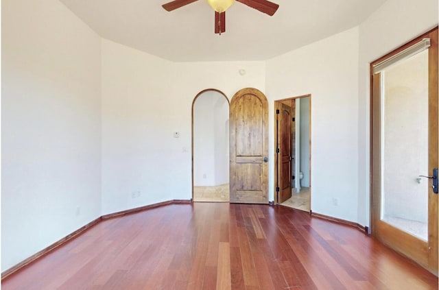 unfurnished room featuring a ceiling fan, arched walkways, baseboards, and wood finished floors