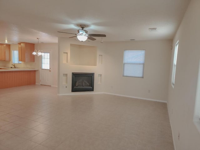 unfurnished living room featuring ceiling fan with notable chandelier, light tile patterned flooring, and sink