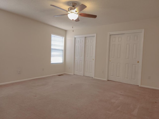 unfurnished bedroom with multiple closets, ceiling fan, and light colored carpet