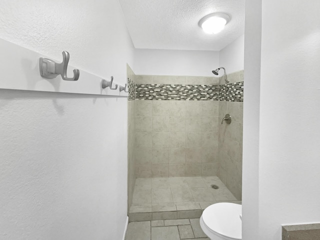 bathroom featuring tile patterned floors, toilet, a tile shower, and a textured ceiling