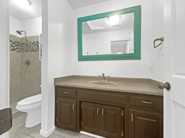 bathroom with tiled shower, tile patterned flooring, vanity, and toilet