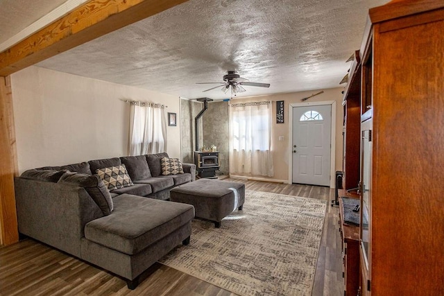 living room featuring ceiling fan, wood-type flooring, a wood stove, and a textured ceiling