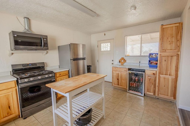 kitchen featuring a textured ceiling, stainless steel appliances, beverage cooler, and light tile patterned flooring