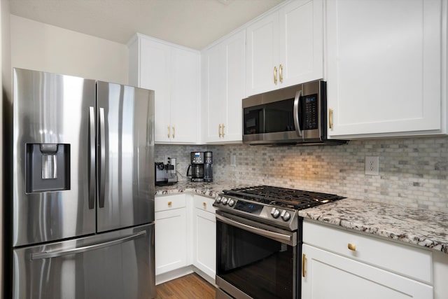 kitchen featuring white cabinets, appliances with stainless steel finishes, light stone countertops, and backsplash