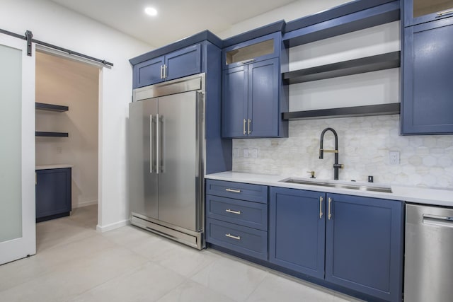 kitchen featuring blue cabinets, sink, decorative backsplash, a barn door, and appliances with stainless steel finishes