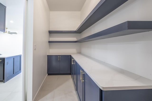 bar featuring blue cabinetry, light stone countertops, light tile patterned floors, and ceiling fan