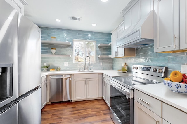 kitchen with sink, stainless steel appliances, white cabinets, custom range hood, and hardwood / wood-style flooring