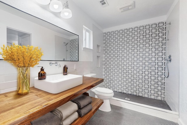 bathroom featuring toilet, sink, tile walls, and tiled shower