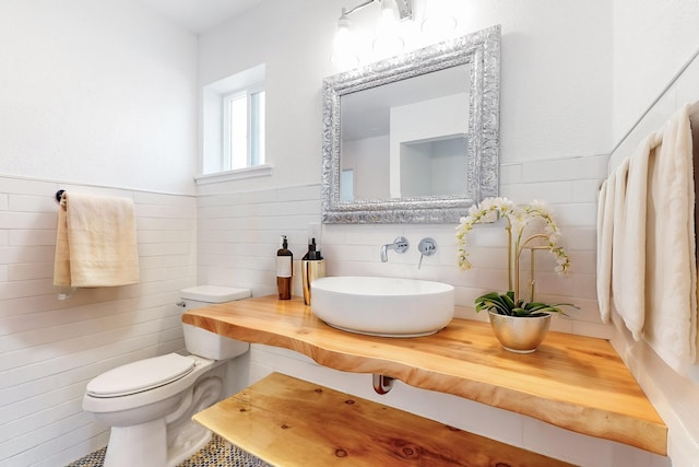 bathroom with toilet, sink, and tile walls