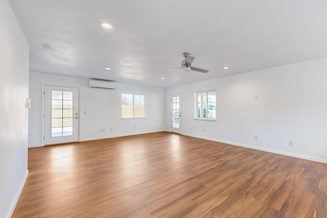 empty room with a wall mounted air conditioner, ceiling fan, and light wood-type flooring