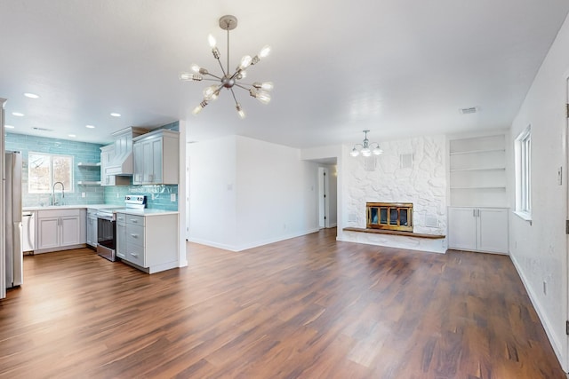 kitchen with sink, a notable chandelier, dark hardwood / wood-style floors, a stone fireplace, and stainless steel electric range