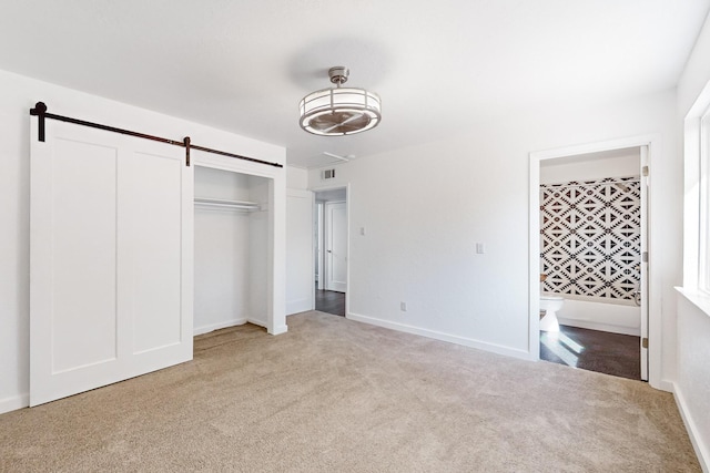 unfurnished bedroom with a barn door, light colored carpet, and a closet