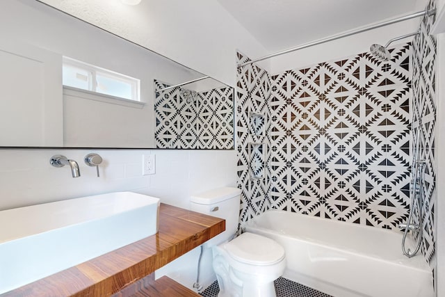 full bathroom with sink, tiled shower / bath combo, toilet, and tile walls