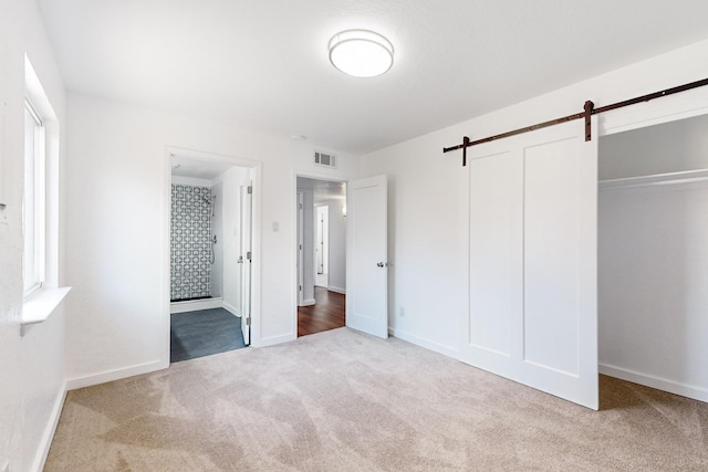 unfurnished bedroom featuring a barn door, light colored carpet, and a closet