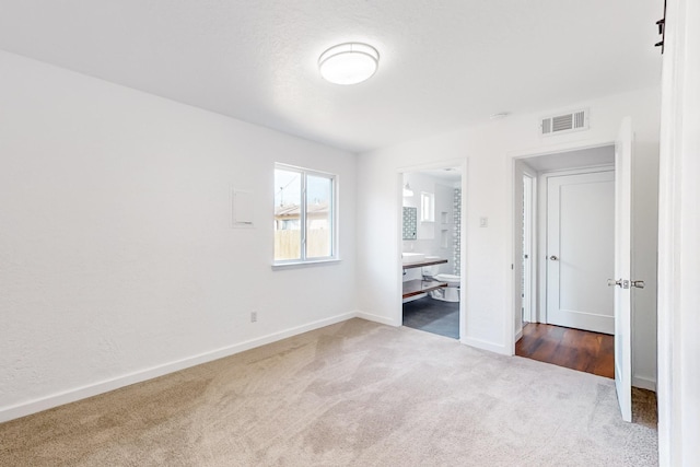 unfurnished bedroom featuring ensuite bath and carpet floors