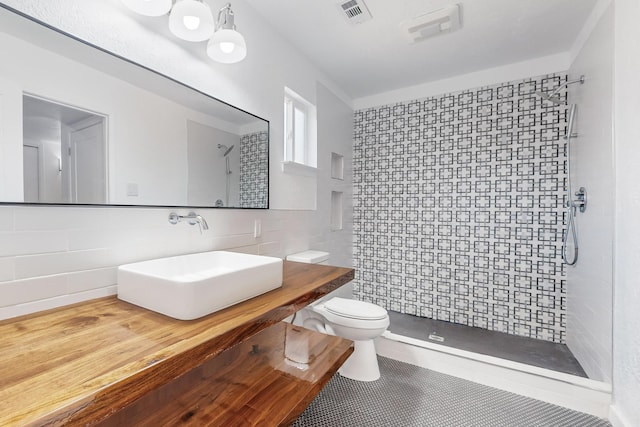 bathroom featuring tile patterned floors, sink, toilet, tile walls, and a tile shower