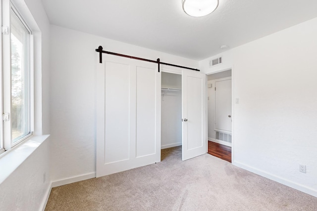 unfurnished bedroom with a barn door, light colored carpet, and a closet