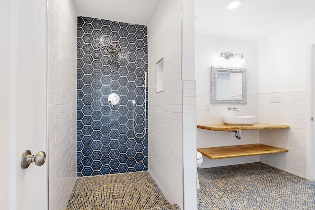 bathroom with tile patterned floors, sink, toilet, tiled shower, and tile walls