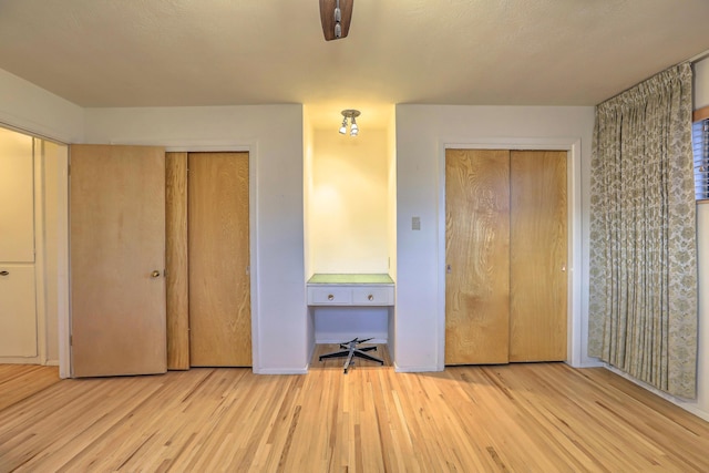 unfurnished bedroom with light hardwood / wood-style flooring and two closets