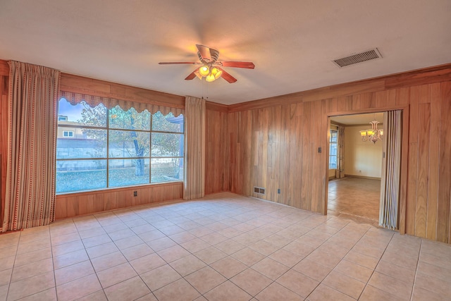 spare room with wooden walls, light tile patterned floors, and ceiling fan with notable chandelier