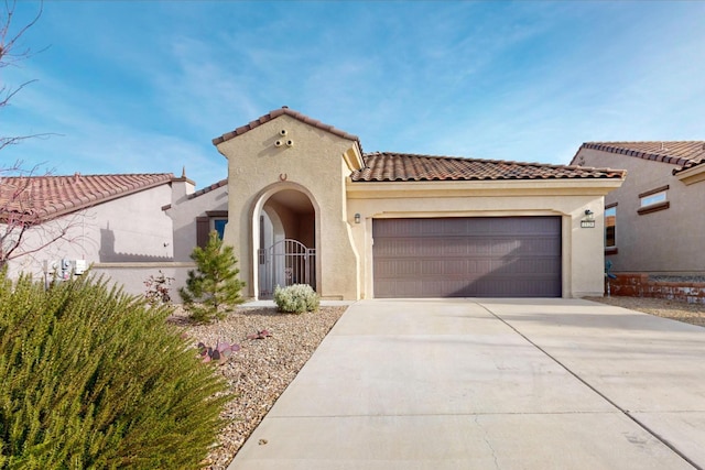 mediterranean / spanish-style home with stucco siding, concrete driveway, an attached garage, a gate, and a tiled roof