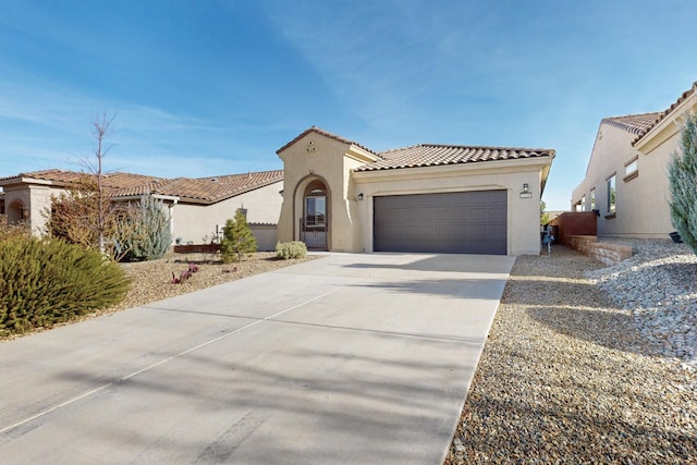 mediterranean / spanish house with an attached garage, a tiled roof, concrete driveway, and stucco siding