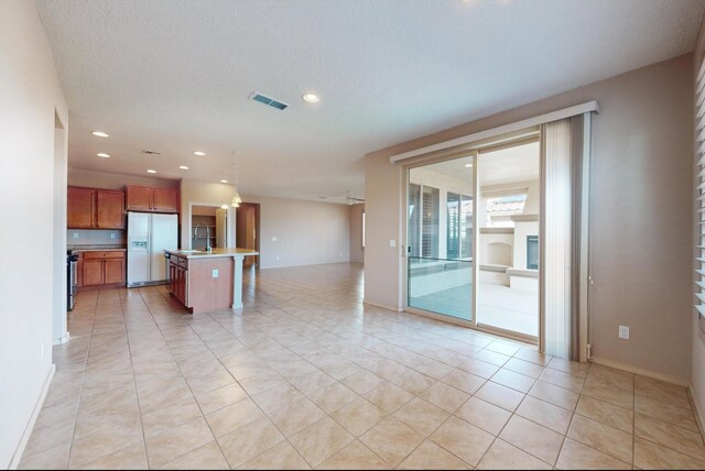 kitchen with sink, white refrigerator with ice dispenser, a breakfast bar area, a kitchen island with sink, and light tile patterned flooring